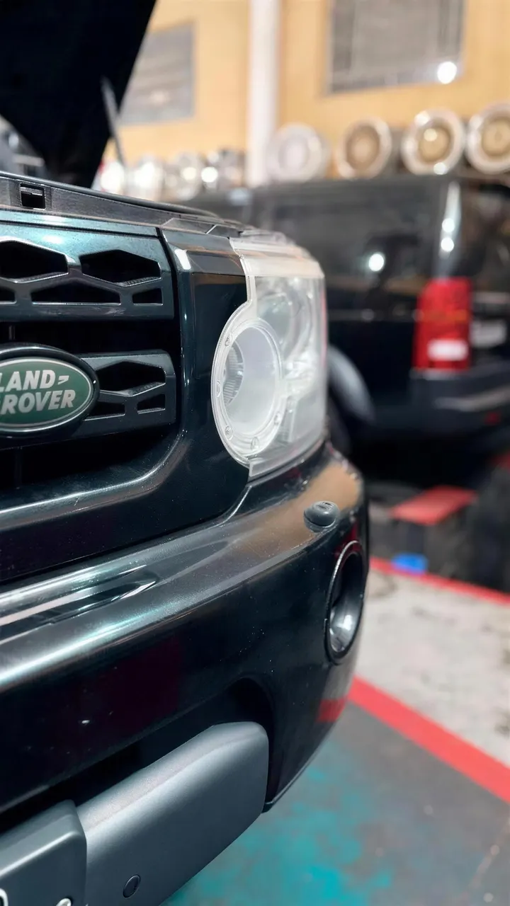 Frente de um Land Rover preto de capô aberto, dentro da oficina