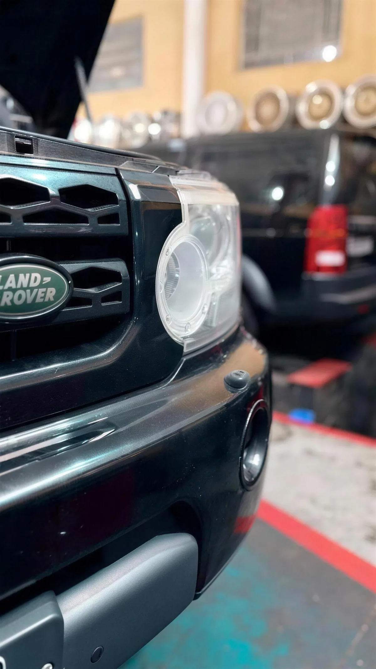 Frente de um Land Rover preto de capô aberto, dentro da oficina