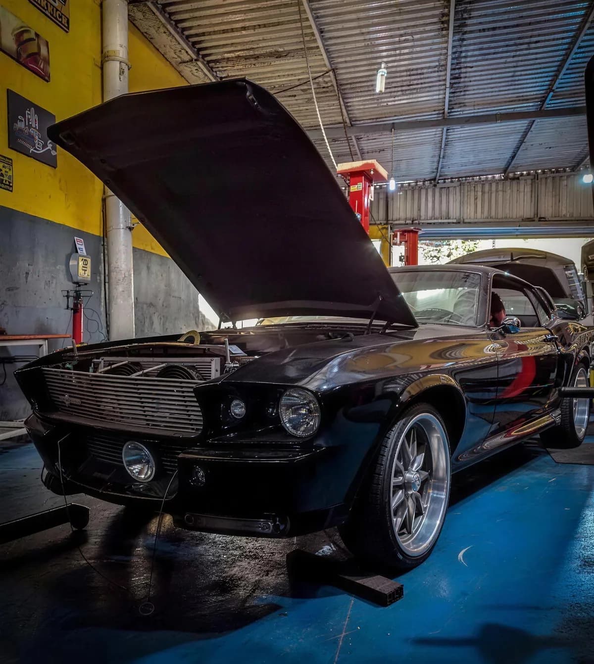Mustang clássico preto de capô aberto, sobre cavaletes no salão da oficina